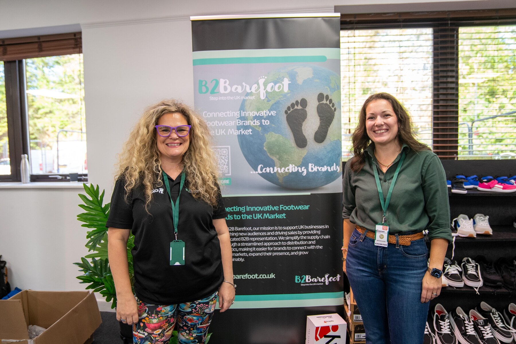 Two exhibitors beside the B2Barefoot banner and shoe display, photo by Barefoot Brit Expo
